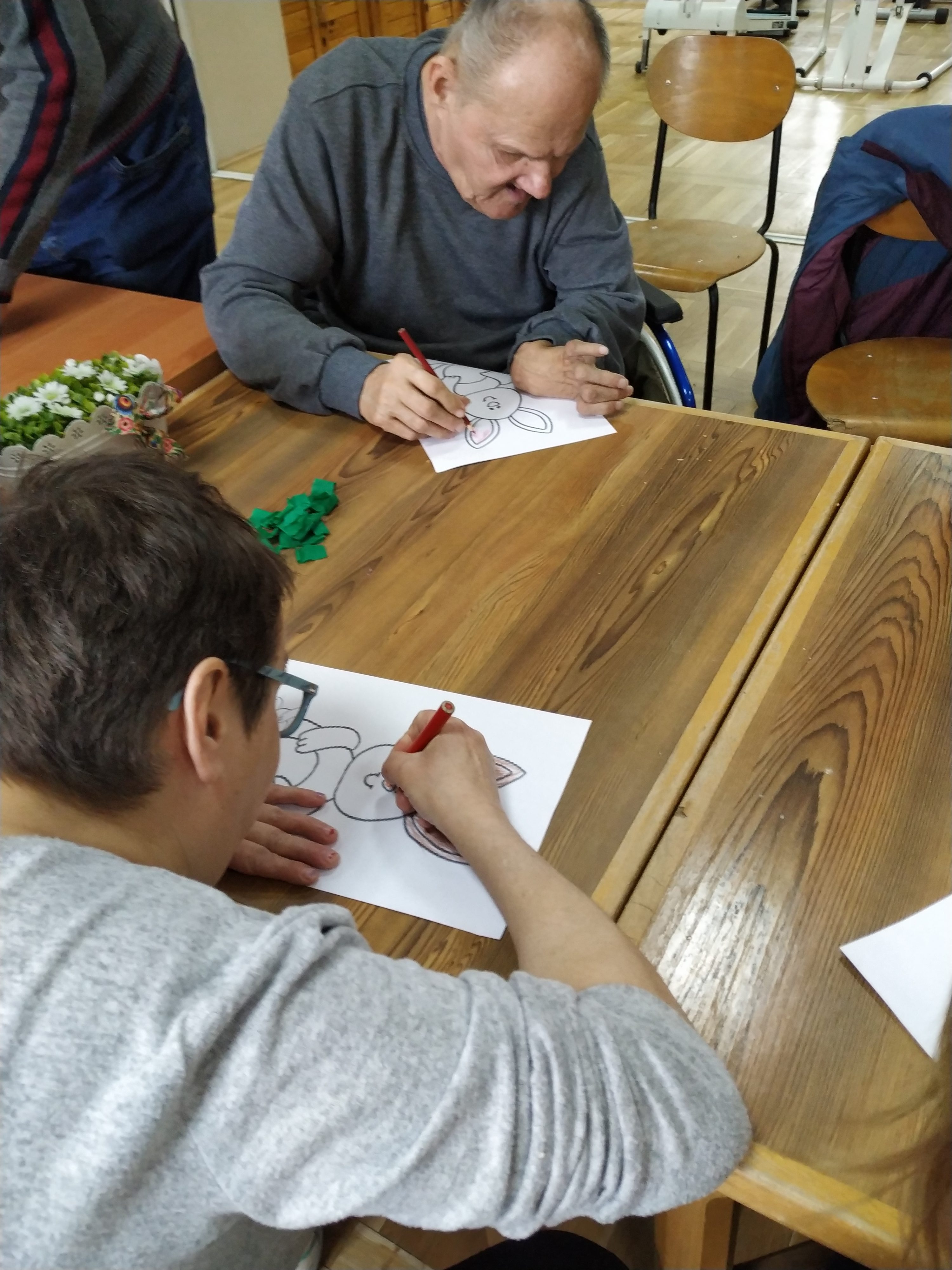 Siedzący razem przy połaczonych stołach mieszkańcy Domów Pomocy Społecznej w Chojnie i Nowej Wsi rysują kredkami wielkanocne zające.