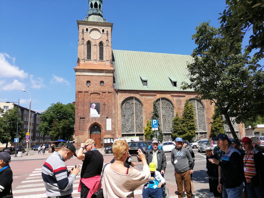 Grupa mieszkańców Domu Pomocy Społecznej w Chojnie stojąca na chodniku przed kościołem św. Barbary w Gdańsku.
