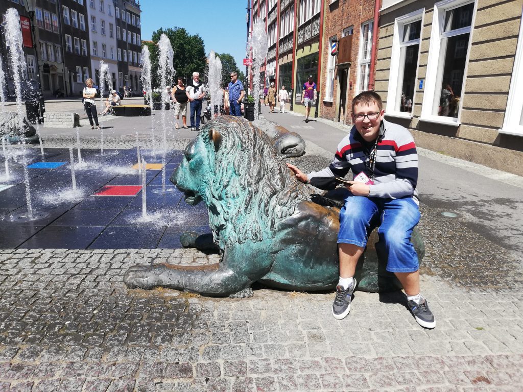 Mieszkaniec Domu Pomocy Społecznej w Chojnie pozuje do zdjęcia przy fontannie i rzeźbach gdańskich lwów.