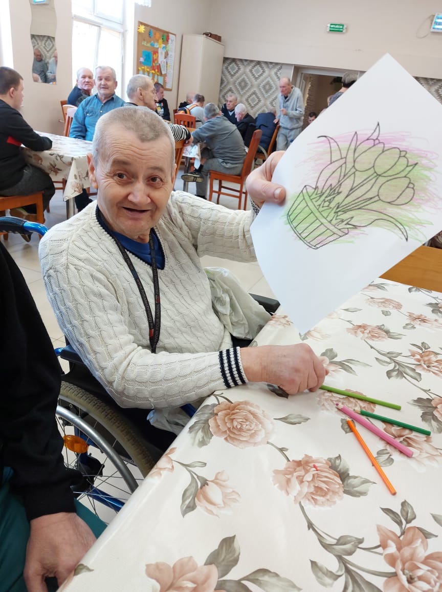 Siedzący na wózku inwalidzkim mieszkaniec Domu Pomocy Społecznej w Chojnie prezentuje wykonaną przez siebie kolorowankę.