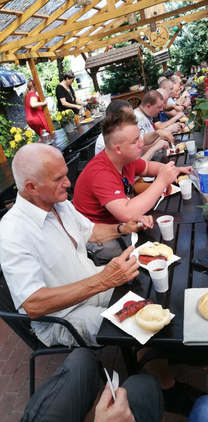 Mieszkańcy Domu Pomocy Społecznej w Chojnie jedzą kiełbasy z grilla przy łączonych stołach.