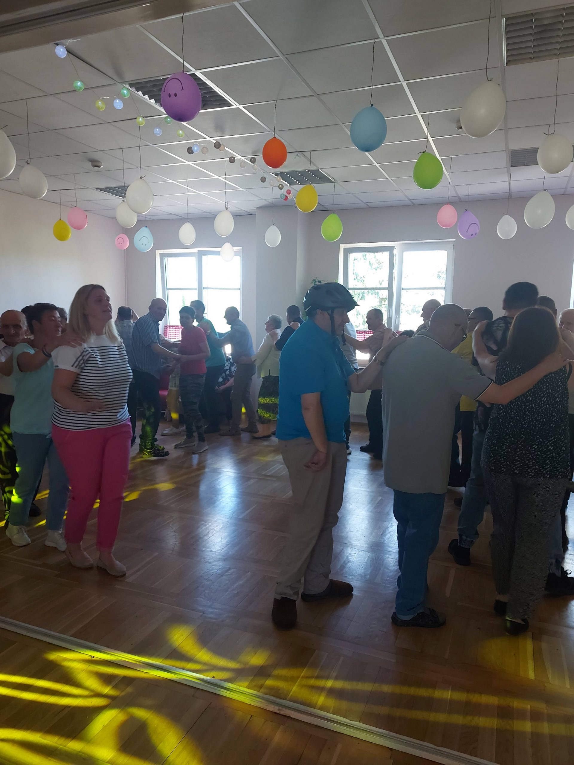 Mieszkańcy domu pomocy społecznej bawią się w kręgu podczas zabawy tanecznej.